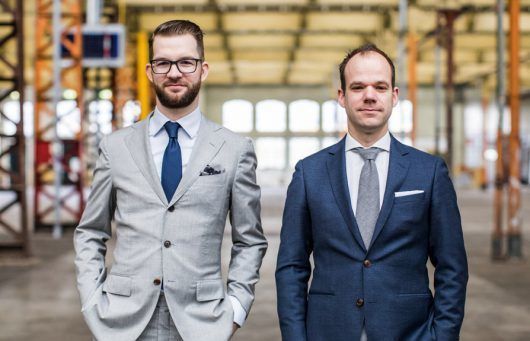 Twee professioneel geklede heren in een industriële omgeving voor een advocatenkantoor.