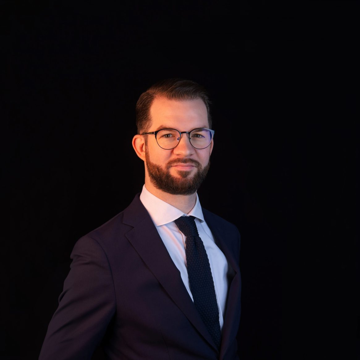 Formele man met bril, baard en donker pak, professioneel portret.
